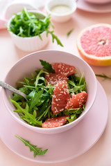 Fresh citrus salad with arugula, grapefruit and sesame seeds on pink background. Selective  focus. Raw vegetarian spring detox food.