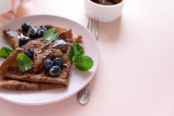 Homemade chocolate crepes served with blueberries, sauce and mint leaves on pink background. Selective focus. Top view. Copy  space