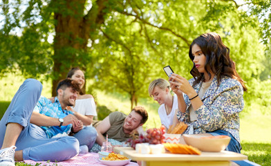 leisure, technology and people concept - woman using smartphone at picnic with friends in summer...