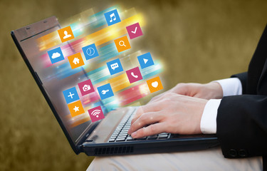 Hand using laptop with colorful fast moving application icons and symbols concept
