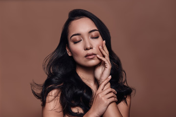 Sensual touch. Beautiful young woman keeping eyes closed while standing against brown background