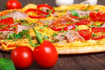 Close up Italian pizza with ham, cheese, pepper and herbs on a brown table decorated by mushrooms, red sweet pepper and cherry tomatoes