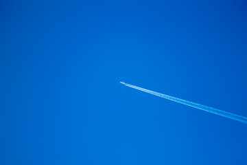alone airplane flying in clear blue sky with white condensation trails