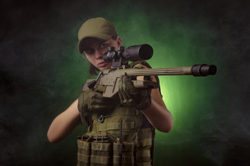 the girl in military special clothes posing with a gun in his hands on a dark background in the haze