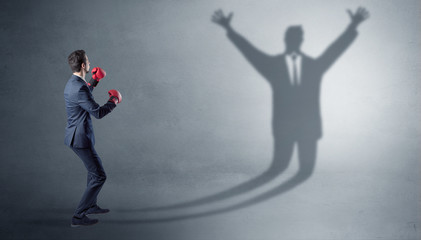 Businessman with boxing gloves fighting with disarmed businessman shadow
