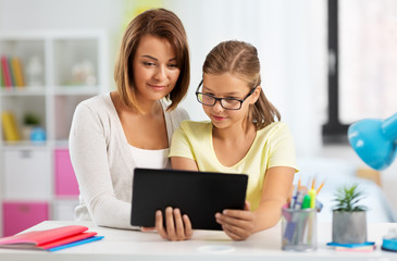 education, family and learning concept - mother and daughter with tablet pc computer doing homework together at home