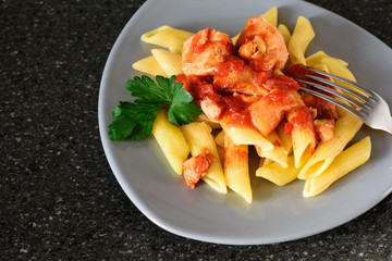 Pasta with salmon in tomato sauce on a gray plate with greens and fork