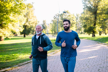 Happy father and son jogging together outdoors in park.