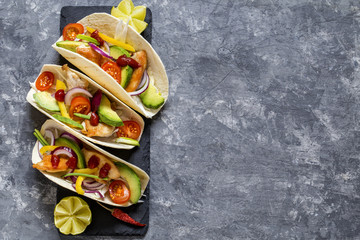 Mexican food tacos, fried chicken, greens,  avocado, pepper, red cabbage and avocado in tortillas on dark background