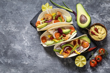 Mexican food tacos, fried chicken, greens,  avocado, pepper, red cabbage and avocado in tortillas on dark background
