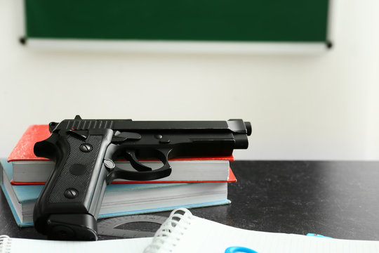 Pistol And Stationery On Table In Classroom. No Guns In School