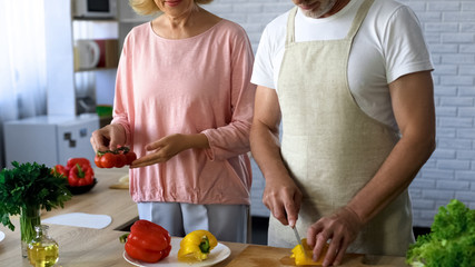 Mature husband and wife cooking vegetarian lunch in kitchen, family traditions