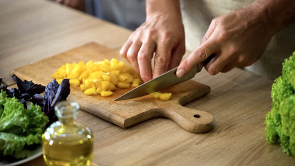 Senior man cutting fresh pepper on chopping board, preparing vegetarian salad