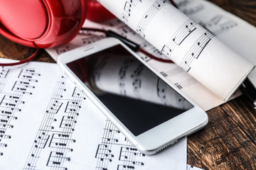 Mobile phone, headphones and music sheets on table