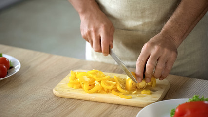 Senior male cooking vegetarian salad home, man cutting fresh pepper on board