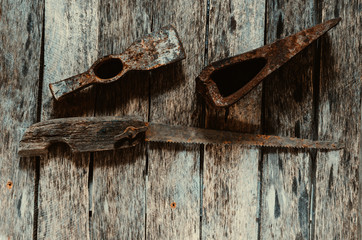 Old rusted hammer, cleaver and hacksaw with wooden handle on wooden background.
