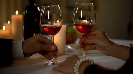 Husband and wife hands holding red wine glasses, tender feelings, toasting
