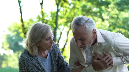 Old man having sudden heart attack during walk in park, wife helping him, care