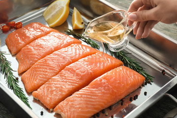 Woman pouring raw salmon fillet with oil