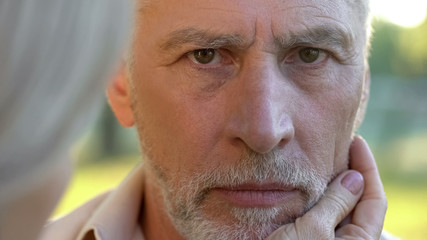 Sad retired man looking into camera, woman supporting husband, close-up view
