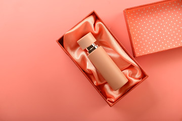 Box with bottle of perfume on coral background