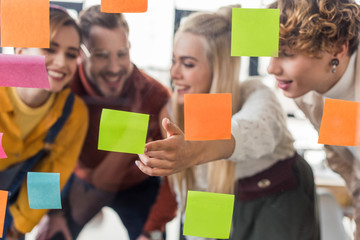 female and male casual businesspeople through glass window with colorful sticky notes in office