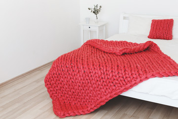 Red merino wool blanket or plaid on bed with white linen. Blanket of thick yarn. Chunky knit.