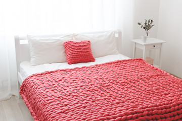 Red merino wool blanket or plaid on bed with white linen. Blanket of thick yarn. Chunky knit. Bedroom interior decor.