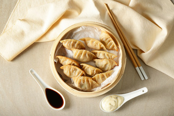 Bamboo steamer with tasty Japanese gyoza and sauces on light table