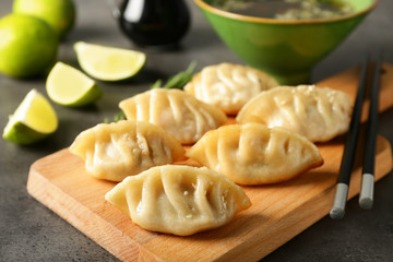 Wooden board with tasty Japanese gyoza on grey table