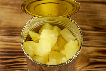 Opened tin can of pineapple pieces on wooden table