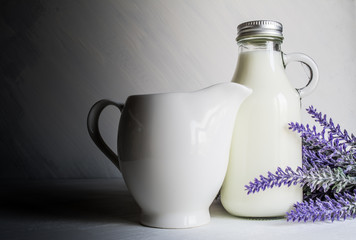 Fototapeta na wymiar Vintage bottle with milk, next to a beautiful jug and a branch of lavender flowers on a white vintage background