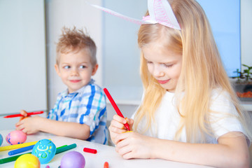 Little girl and boy in rabbit bunny ears on head are preparing for Easter and painting eggs. Colorful markers. Easter, family and holidays concept