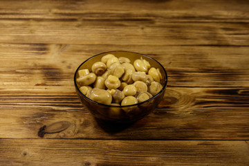 Glass bowl with pickled champignons. Marinated mushrooms on wooden table