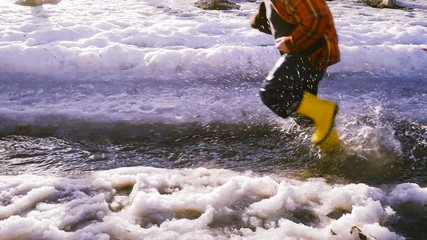 Kid running at the spring creek with melting ice