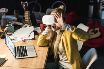 excited casual businesswoman gesturing with hands while having virtual reality experience at computer desk in office