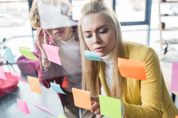 casual businessman and businesswoman putting colorful sticky notes on glass window in office