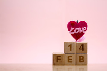 Wooden blocks of date 14 Feb for February on pink background with heart and word LOVE. Love and valentine's day concept