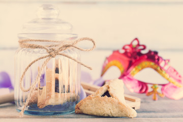 Jewish Hamantaschen homemade biscuits or cookies in a glass jar with purim mask and purim gragger