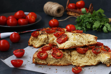 Pieces of focaccia with cherry tomatoes are located close-up on parchment on a dark background