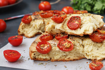 Pieces of focaccia with cherry tomatoes are located close-up on parchment on a dark background
