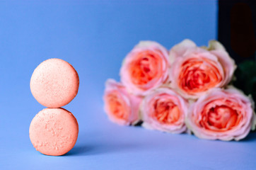 Fototapeta na wymiar Two macaroons and a bouquet of roses in a fashionable coral color.