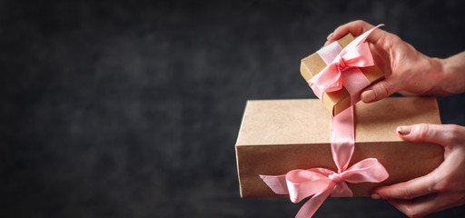 Hands holding Holiday gift boxes Packed in Kraft paper with pink ribbon on dark wooden background.