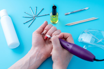 Female manicurist doing a professional manicure hardware using milling cutter on the background of...