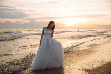 Fototapeta na wymiar Romantic bride in white dress on ocean beach at sunset time. Young beautiful bride on wedding day