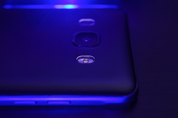 Close-up of the lens of the camera phone in black colour with  creative lighting is a deep dark blue. Macro horizontal photography