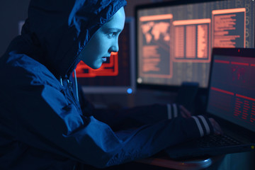 Girl hacker in a hood typing program code while committing a cybercrime hacking a system on the...