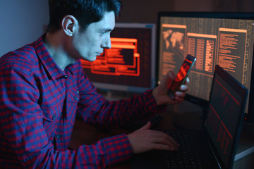 Hacker holding the phone in his hands trying to hack the mobile device cloud and steal data in the...