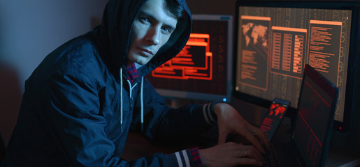 Man in the hood looking in the camera. Hacker attacks and online fraud in the dark on the screen background in neon