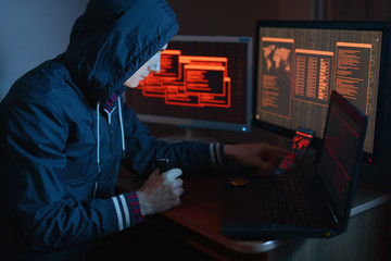Hacker in the hood is pointing his finger at the display indicating the location of the cyberattack in neon light